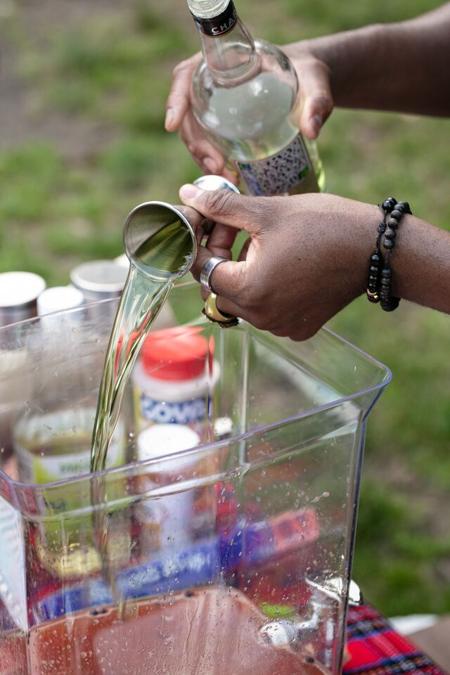 Two hands holding bottle of liquor and measuring cup. Alcohol being pouted into large container with other drinking ingredients