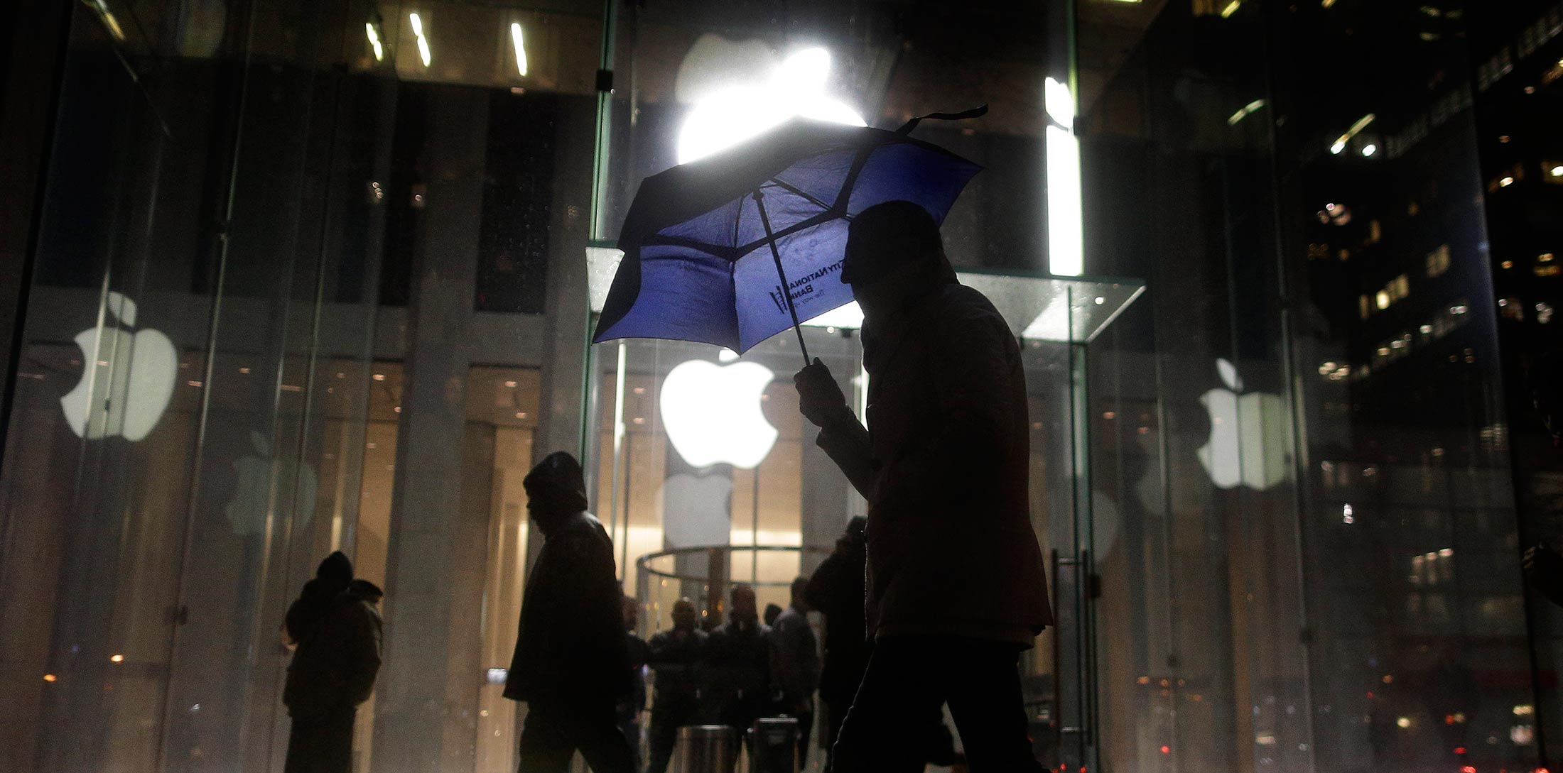 pedestrian walks by the Apple Store on Fifth Avenue while avoiding a small demonstration held along the sidewalk, Tuesday, Feb. 23, 2016, in New York. Protesters assembled in more than 30 cities around the world to lash out at the FBI for obtaining a court order that requires Apple to make it easier to unlock an encrypted iPhone used by a gunman in December's mass murders in California.
