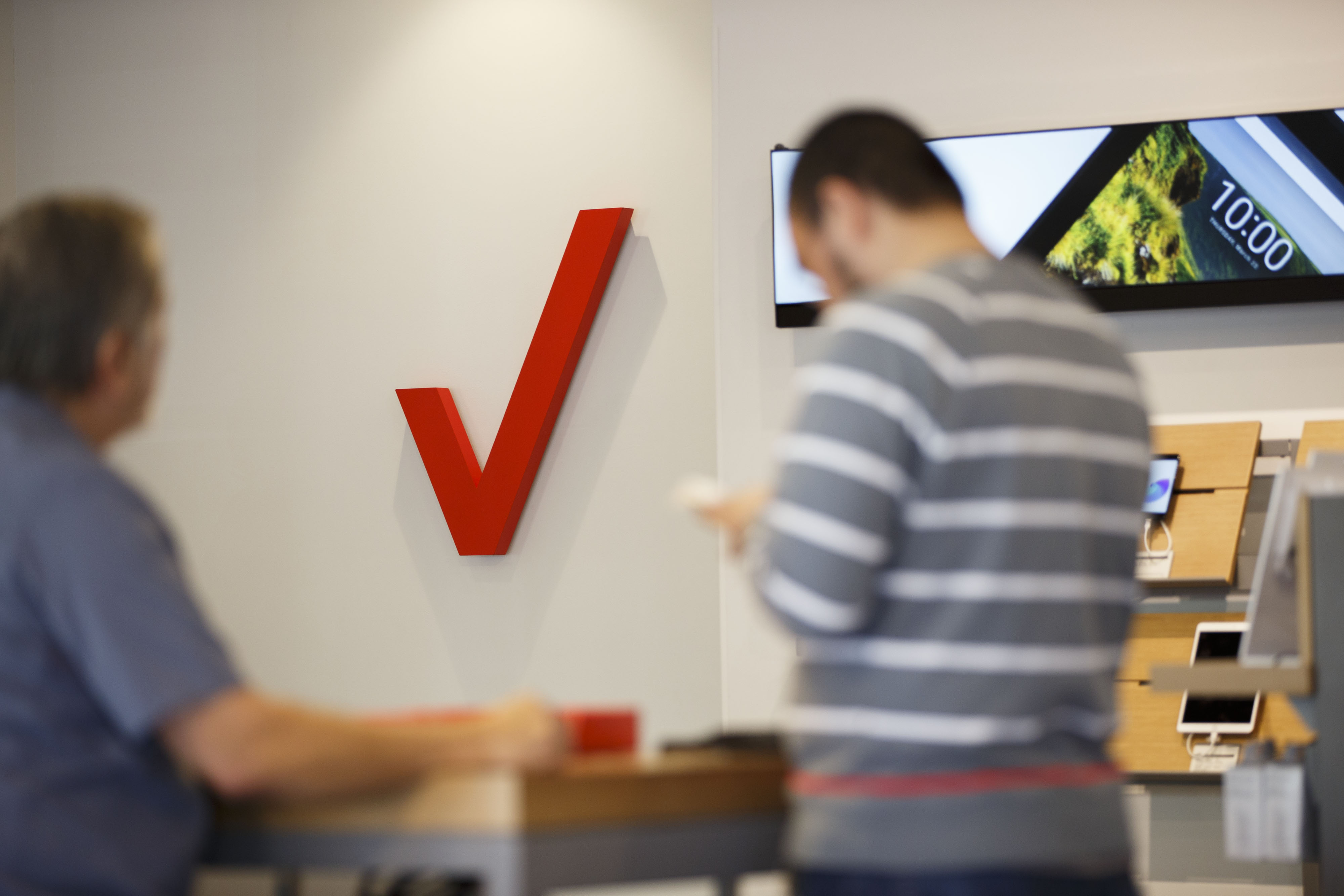 An employee assists a customer in front of a Verizon Communications Inc. logo at a store in Brea, California.