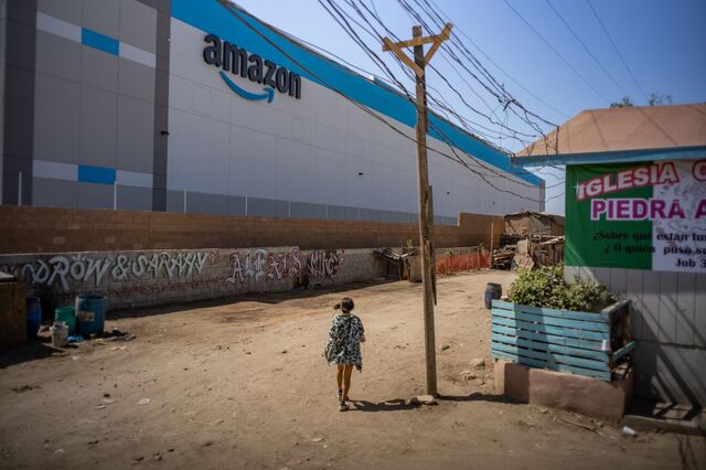 A child passes in front of an Amazon fulfillment center under construction at RMSG Alamar Industrial Park in Tijuana, Mexico, on Friday, Sep. 10, 2021. This month, Amazon will open a $21 million state-of-the-art warehouse in Tijuana, Mexico, that abuts a housing settlement made of cardboard, tarp, and wood scraps along the Tijuana River, less than three miles from the U.S.-Mexico border, reports Vice Media.