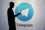 A man is seen as a silhouette as he checks a mobile device whilst standing against an illuminated wall bearing Telegram's logo in this arranged photograph.
