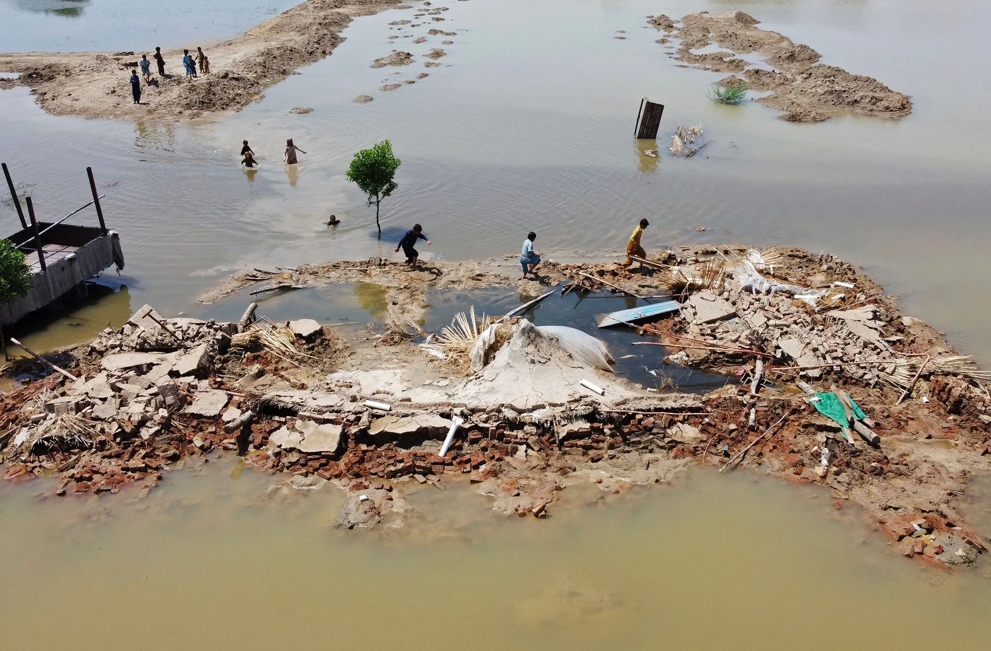 Flood-affected people wading next to a house that collapsed after heavy monsoon rains in Jaffarabad district of Balochistan province.