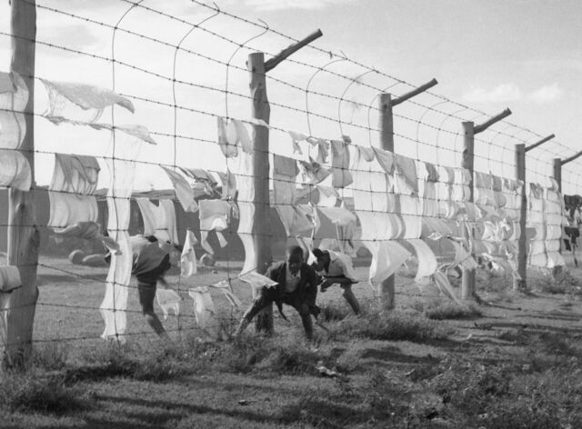 Children climb through a barbed-wire fence separating a Black residential district from a White one, in 1963.