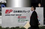Pedestrians walk past signage for Japan Post Group in Tokyo, Japan, on Thursday, Jan. 9, 2020.