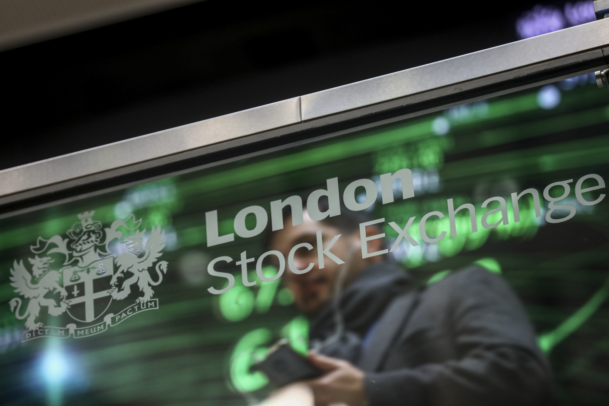 An employee sits reflected in a glass screen featuring the London Stock Exchange Group Plc's logo at their offices in London.