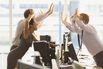 Exuberant business people high-fiving over computers in office