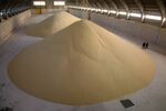 Workers inspect piles of phosphate fertilizer granules in a storage warehouse.