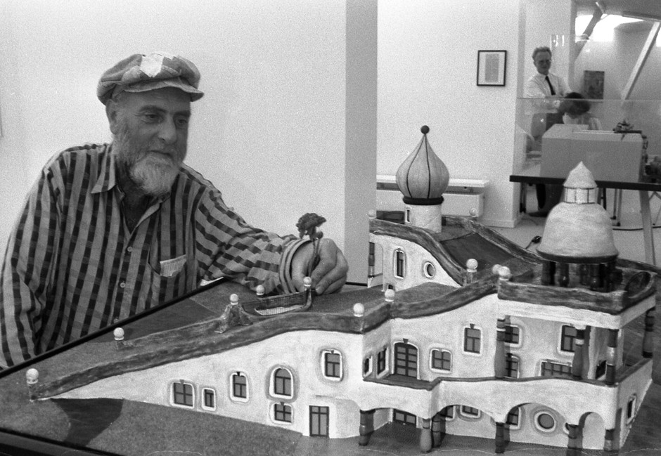 Friedensreich Hundertwasser, sits next to a model of a community center he designed for the city of Frankfurt in 1988.