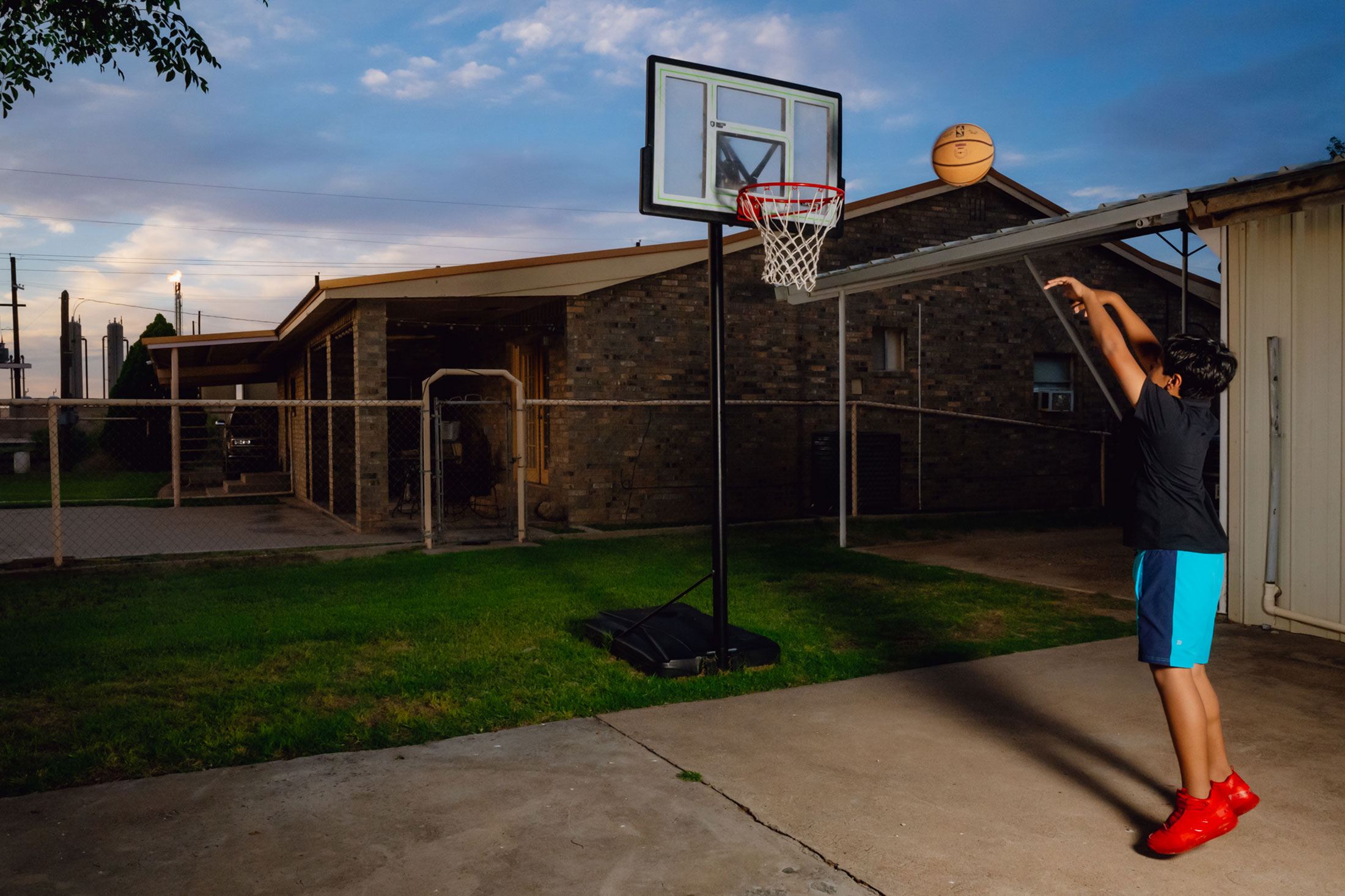 A young resident plays basketball as a gas flare burns nearby in the South Ranchito neighborhood just beyond Odessa, Texas, in May.
