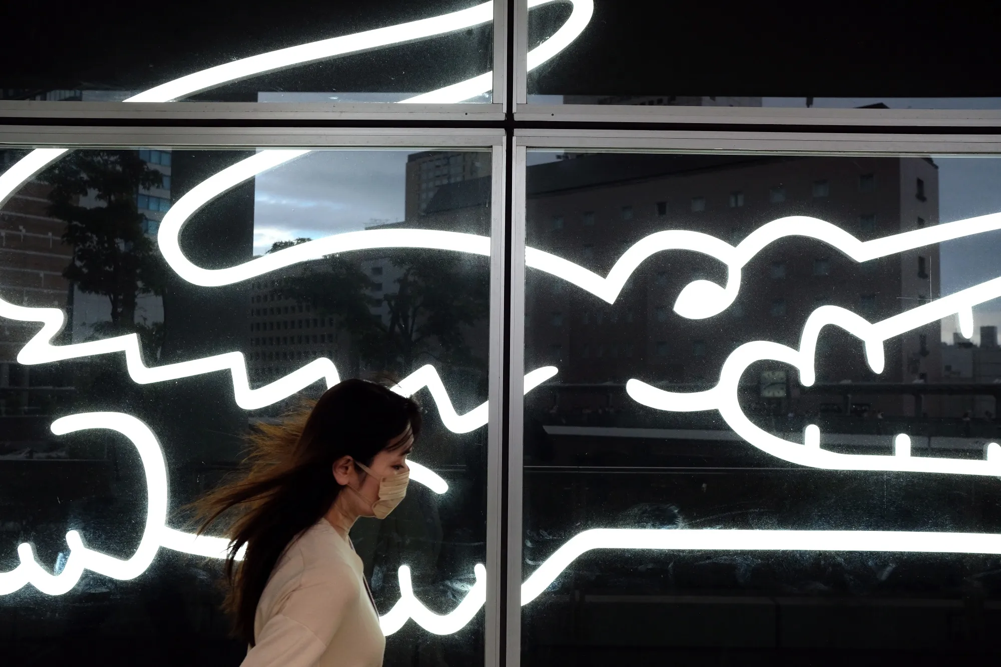 A pedestrian walks past a window display at a Lacoste SA store in Kawasaki, Japan.