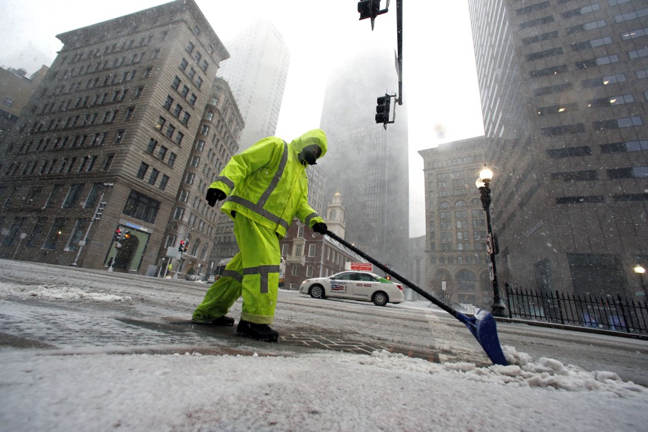 A worker clears snow from a Boston sidewalk during a winter storm Tuesday.