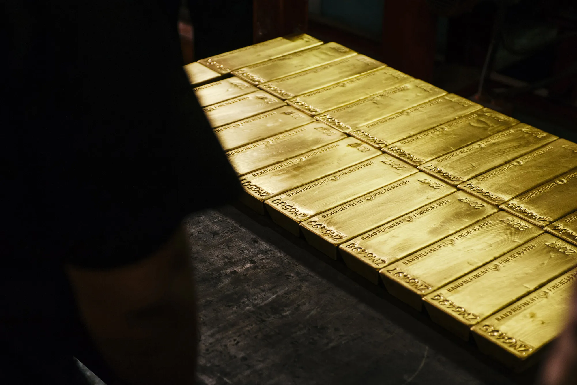 A worker stands beside multiple gold bullion bars following casting at the Rand Refinery Ltd. plant in Germiston, South Africa, on Wednesday, Aug. 16. 2017. Established by the Chamber of Mines of South Africa in 1920, Rand Refinery is the largest integrated single-site precious metals refining and smelting complex in the world, according to their website.
