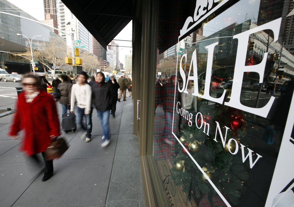 Shoppers walk past a sale sign, painted on a storefront window on Broadway, in New York