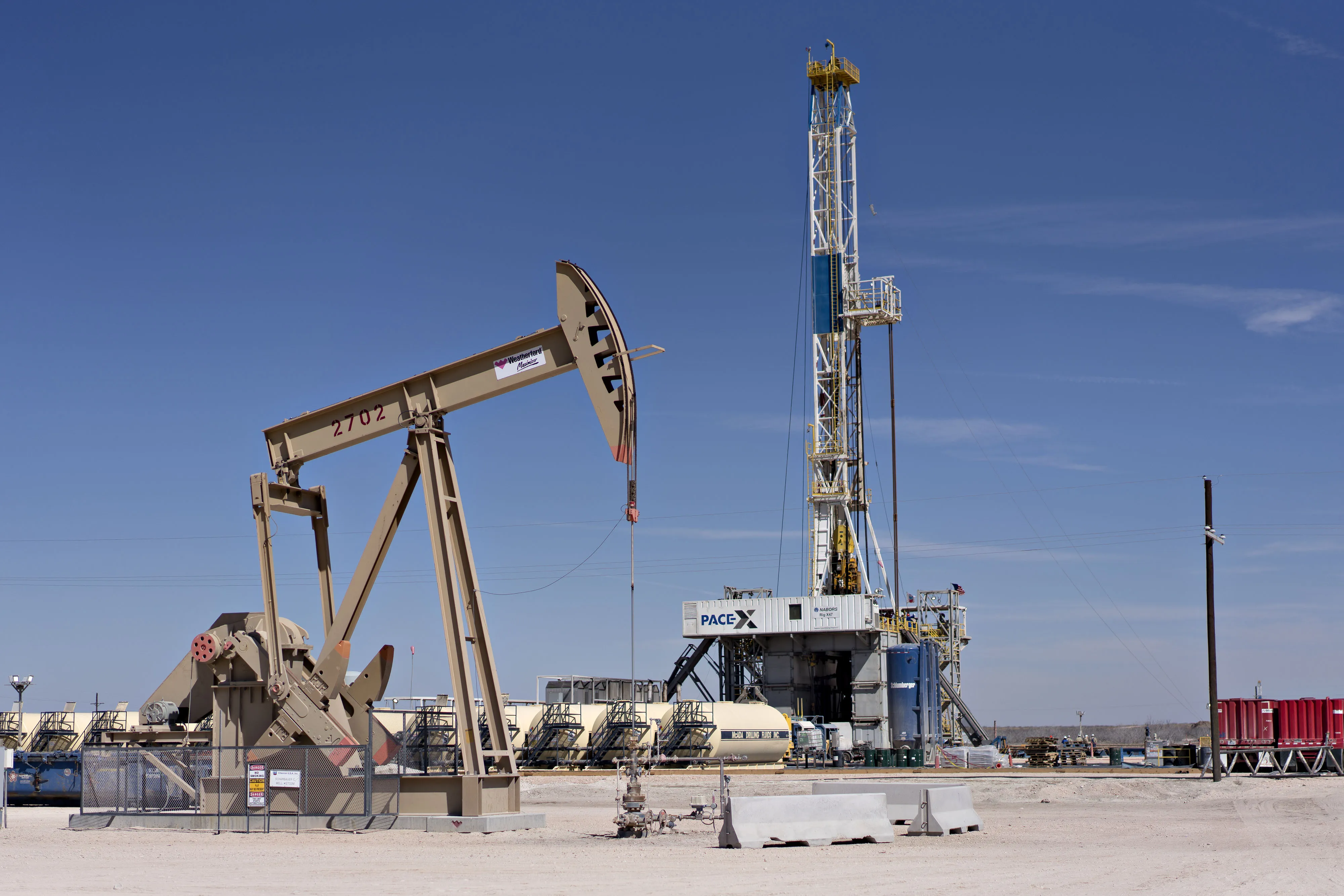 A pumpjack operates near a&nbsp;drill rig standing over an oil well in the Permian Basin near Midland, Texas.
