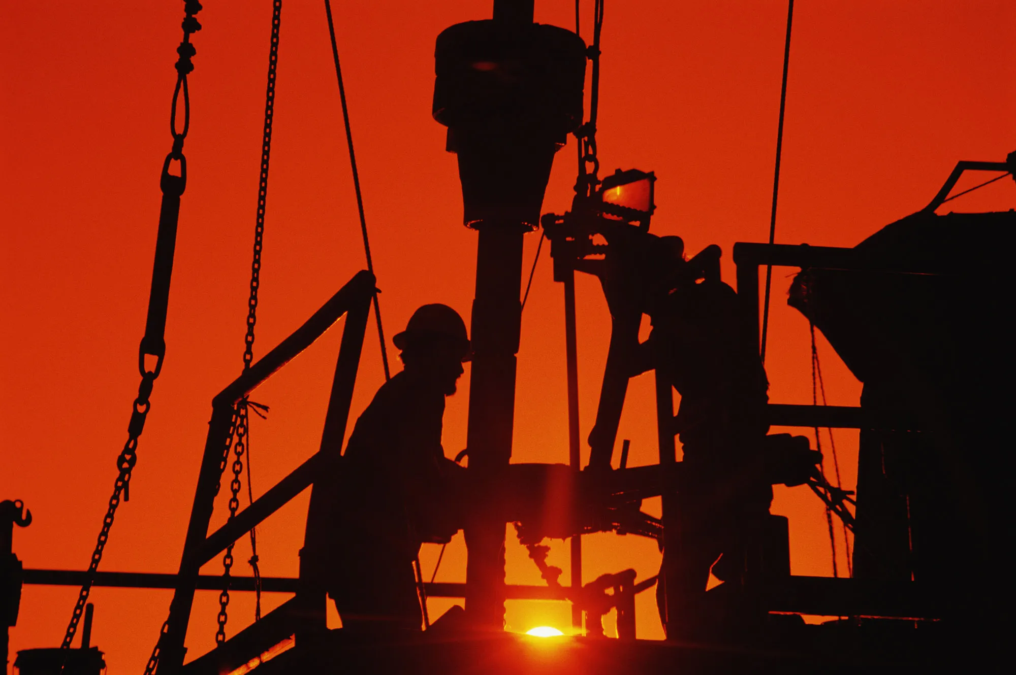 Oil and gas drilling workers on rig, silhouette, sunrise