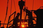 Oil and gas drilling workers on rig, silhouette, sunrise