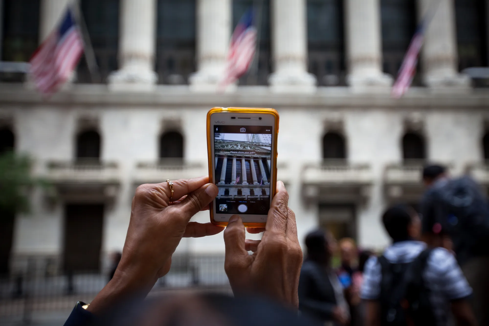 A pedestrian uses a mobile device to take photographs of the New York Stock Exchange.