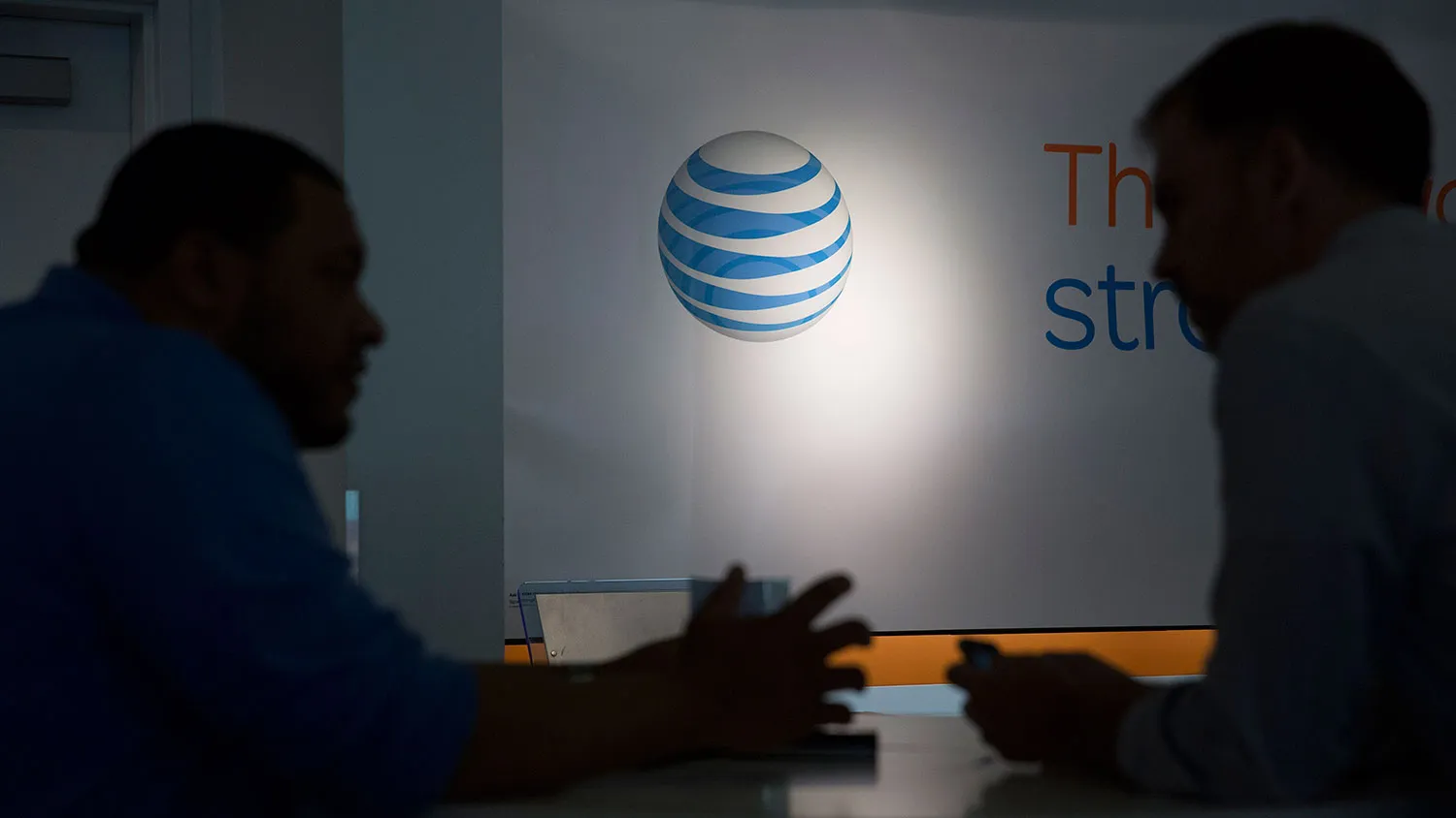 The AT&amp;T Inc. logo is seen past a customer and a retail sales consultant at an AT&amp;T store in Washington on April 21, 2015.
