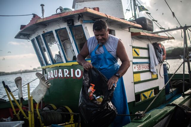 Fisherman Carlos Alberto closes a plastic bag filled with trash that came in his fishing nets after a barely productive fishing morning aside abandoned, rotting ships, boats and seafare structures that float in the Guanabara bay in Sao Gonçalo, Rio de Janeiro.
