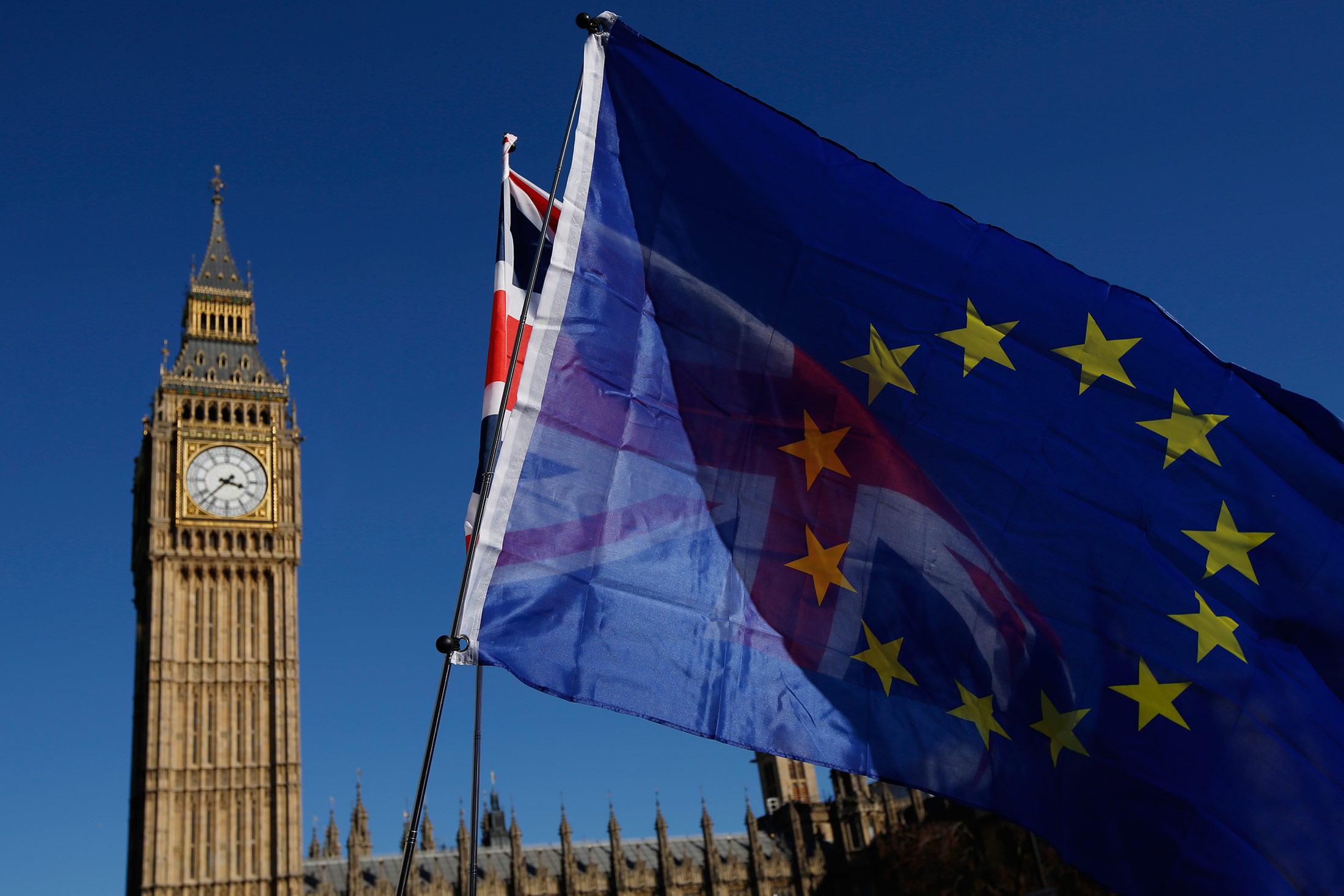 A European Union (EU) flag, front, and a Union flag, also known as Union Jack, fly in front of Elizabeth Tower, commonly referred to as Big Ben, during a Unite for Europe march to protest Brexit in central London, U.K., on Saturday, March 25, 2017. U.K. Prime Minister Theresa May is ready to officially start the process to leave the bloc on March 29.
