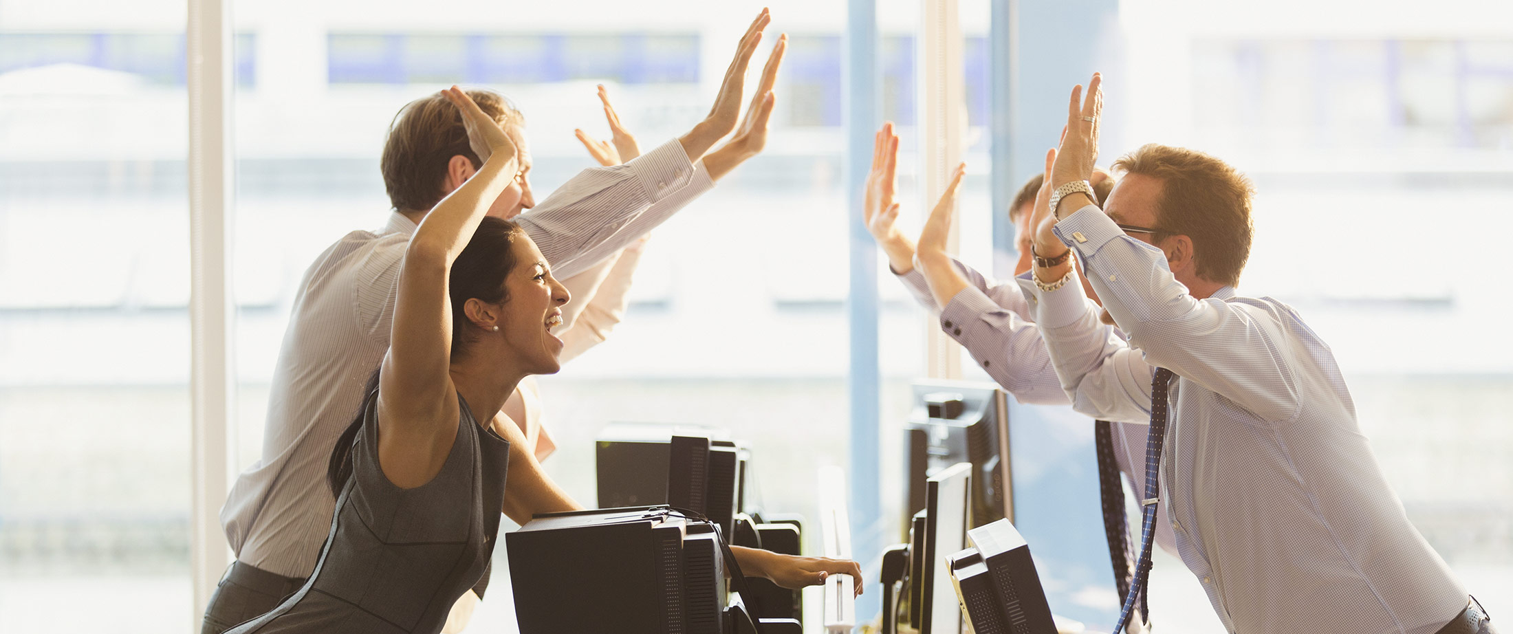 Exuberant business people high-fiving over computers in office
