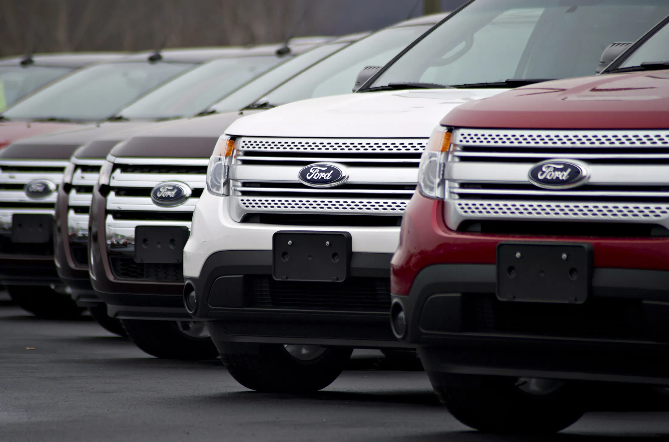 Ford Explorer SUVs sit on display at a car dealership.
