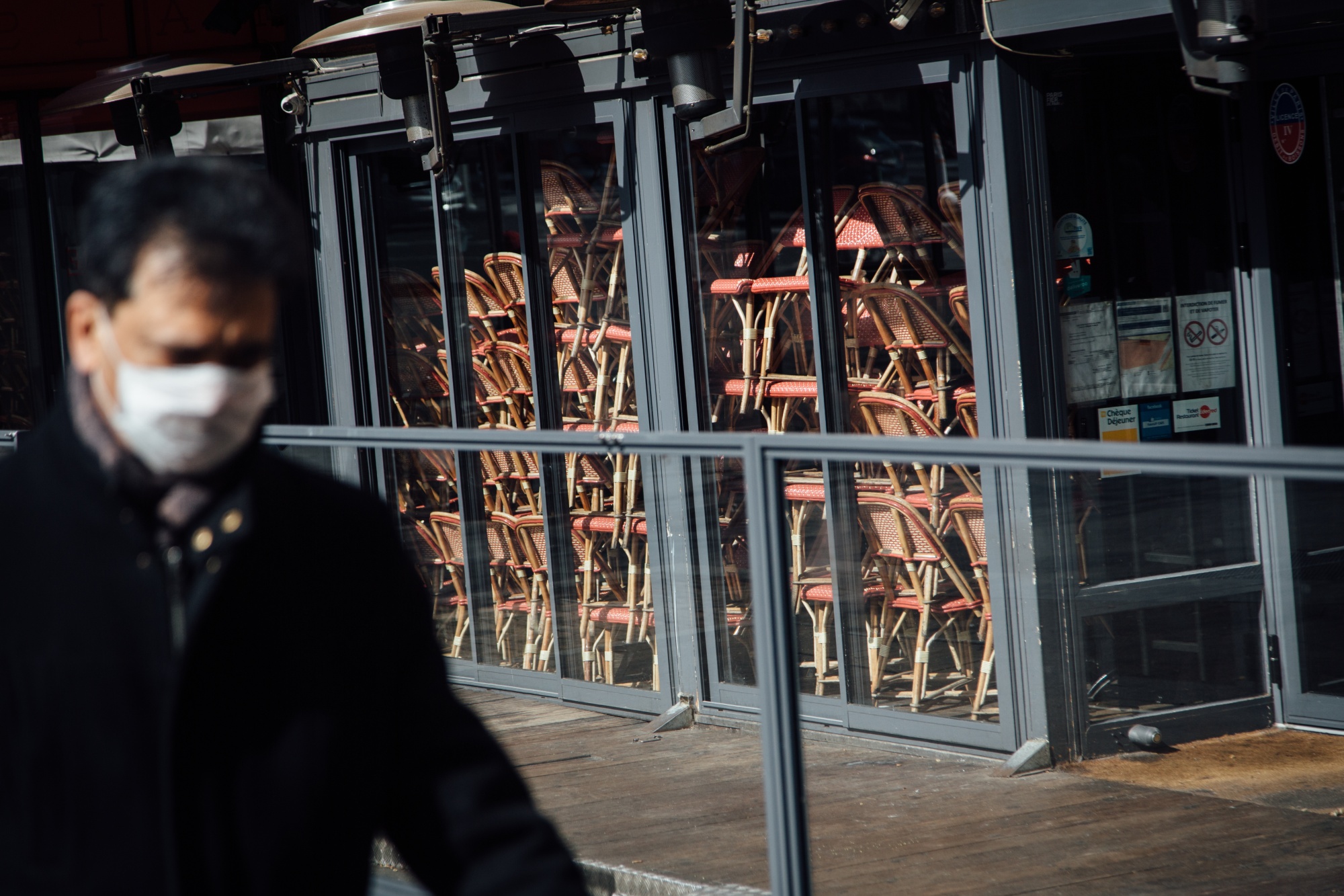 A pedestrian walks past a closed cafe restaurant with chairs stacked inside in Paris.