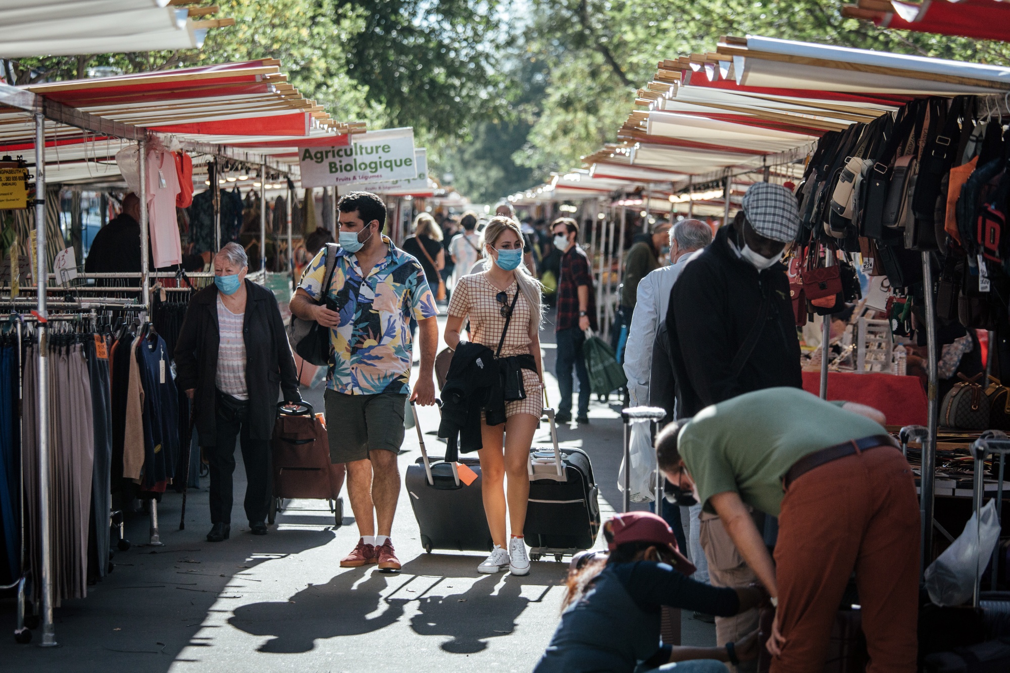 Tourists wearing protective face masks wheel luggage past clothing stalls at the Edgar Quinet market in Paris, France, on&nbsp;Sept. 9.