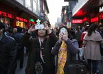 Women take smartphone photos on Qianmen Street in Beijing.
