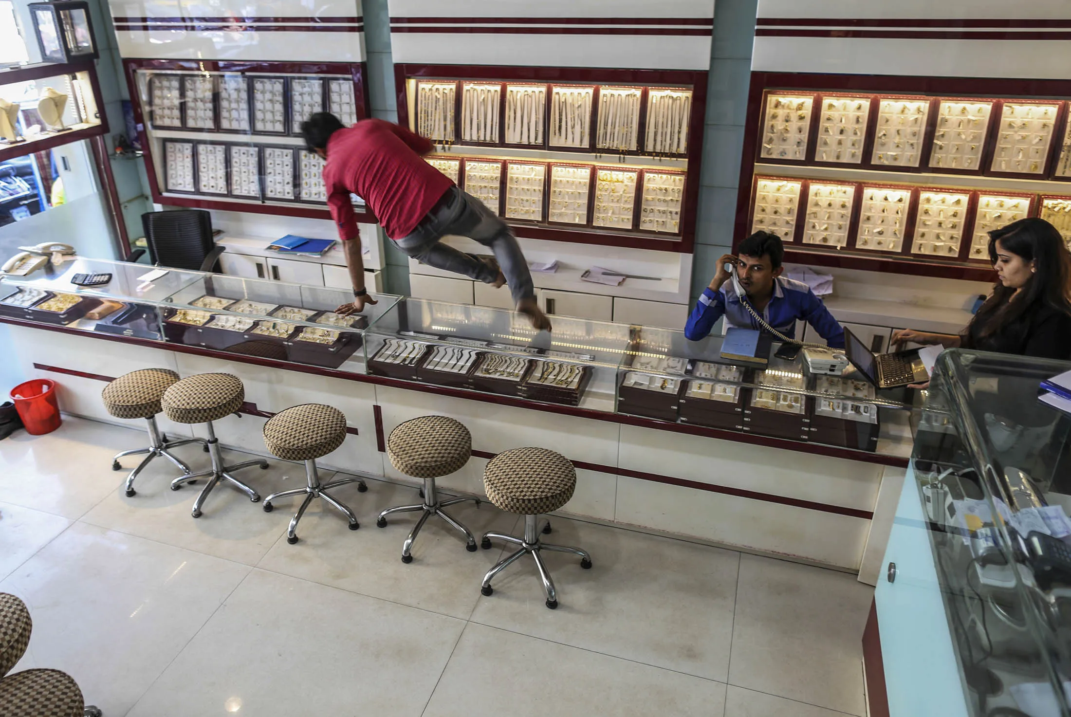 An employee jumps over a display counter as his colleagues wait for customers in Mumbai's Zaveri Bazaar on Nov. 19. Analysts believe that The world’s largest payment networks will see increased transactions following the government’s decision this month to remove high-denomination bills from circulation.
