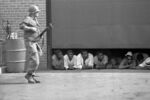 In this July 26, 1967 file photo, an Army soldier stands guard as men captured in the vicinity of the 10th Police Precinct in Detroit peer from under a garage door awaiting transfer.