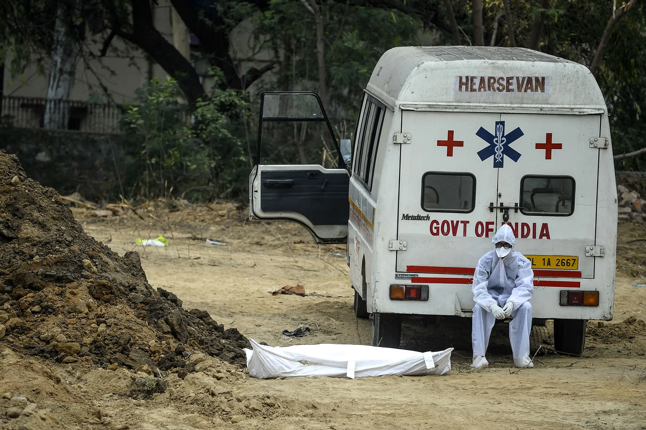 A health worker wearing protective gear sits on an ambulance, next to the a victim who died from the coronavirus, prior to the burial at a graveyard in New Delhi on May 13.