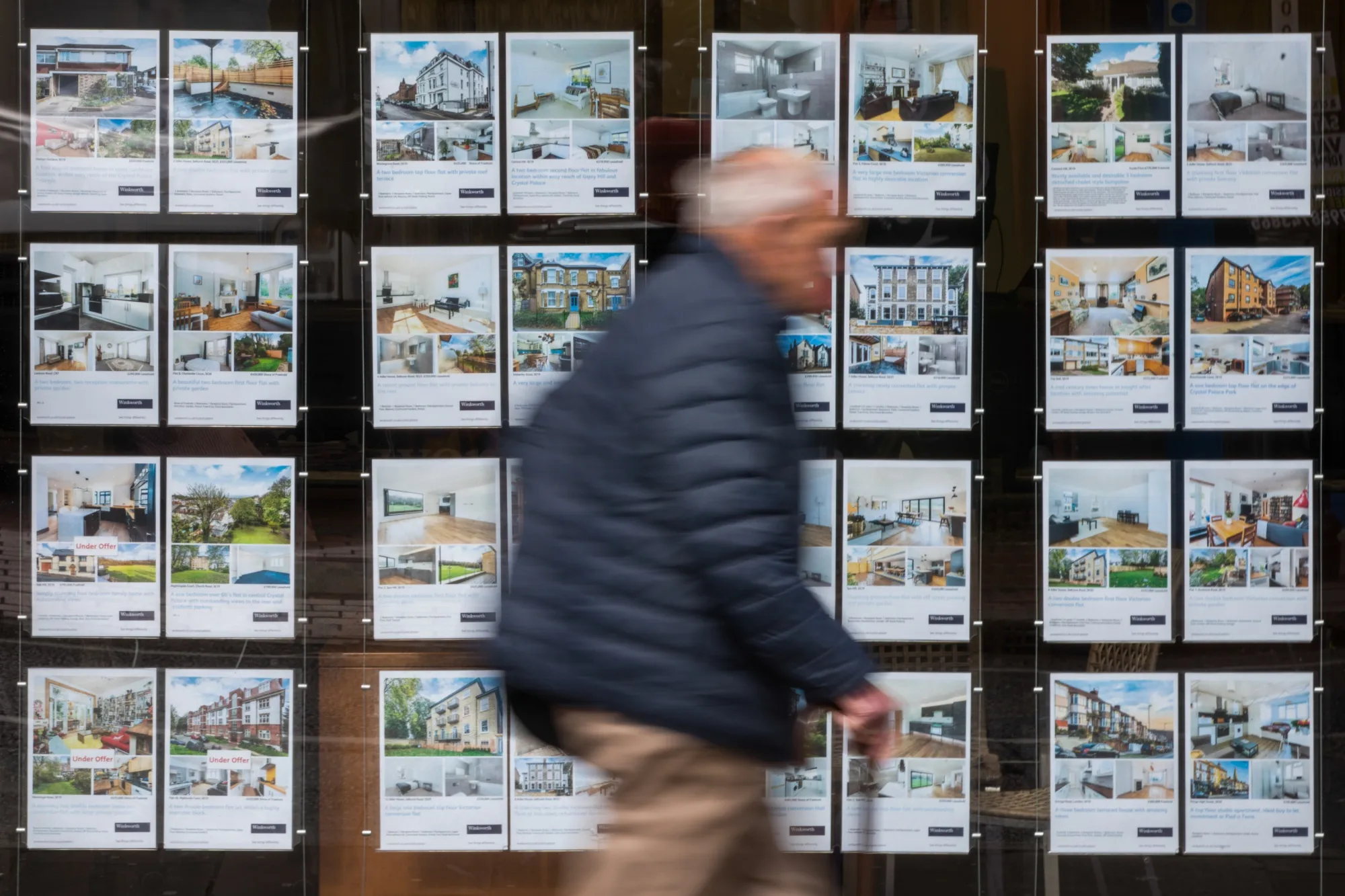 A pedestrian passes an estate agents window advertising properties for sale in London.