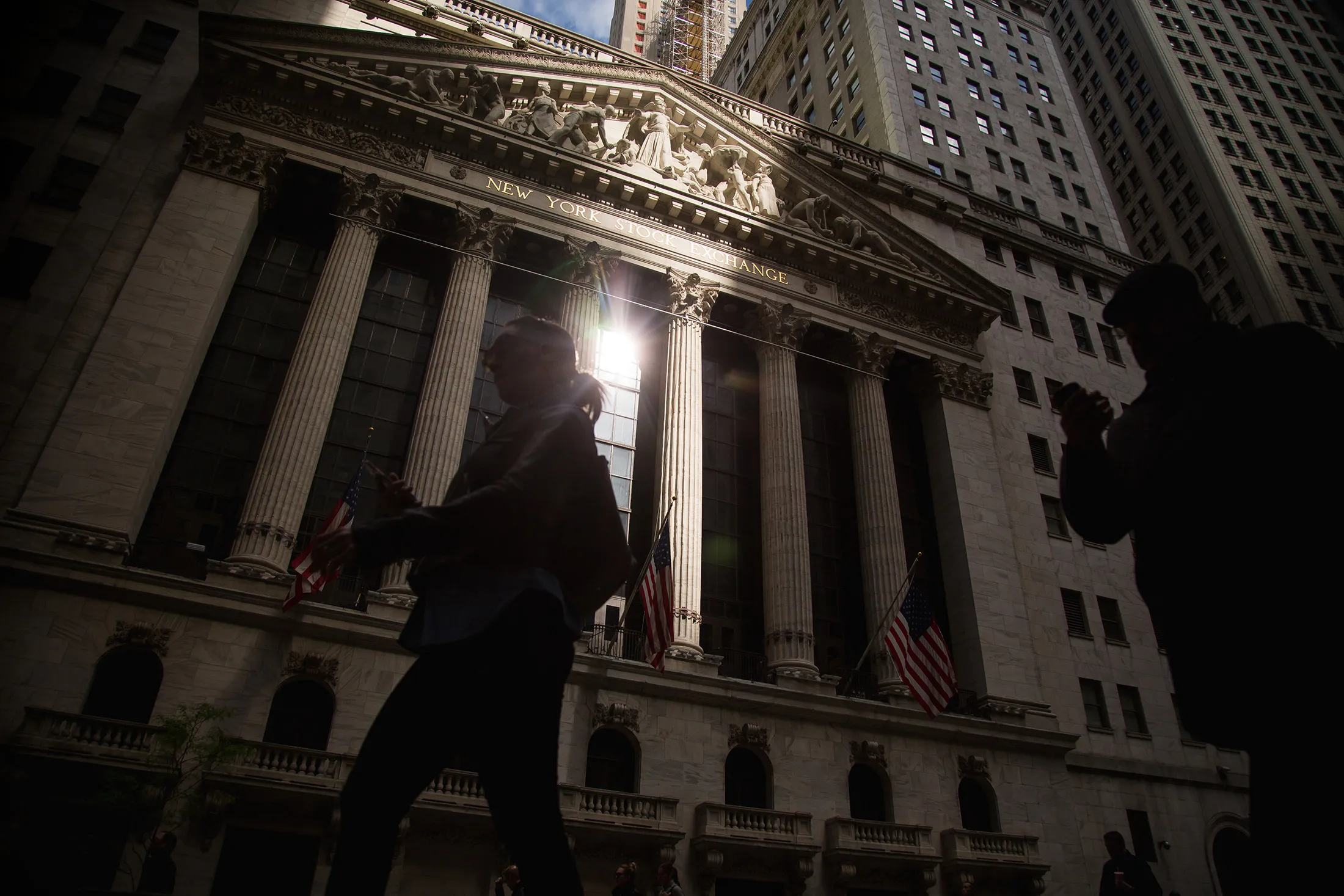 Pedestrians pass in front of the exterior of the New York Stock Exchange (NYSE) in New York, U.S., on Monday, May 16, 2016. Brent crude rose to a six-month high, leading a rebound in commodities and boosting the stocks from the U.S. to developing markets, as supply disruptions in Nigeria added to production woes.
