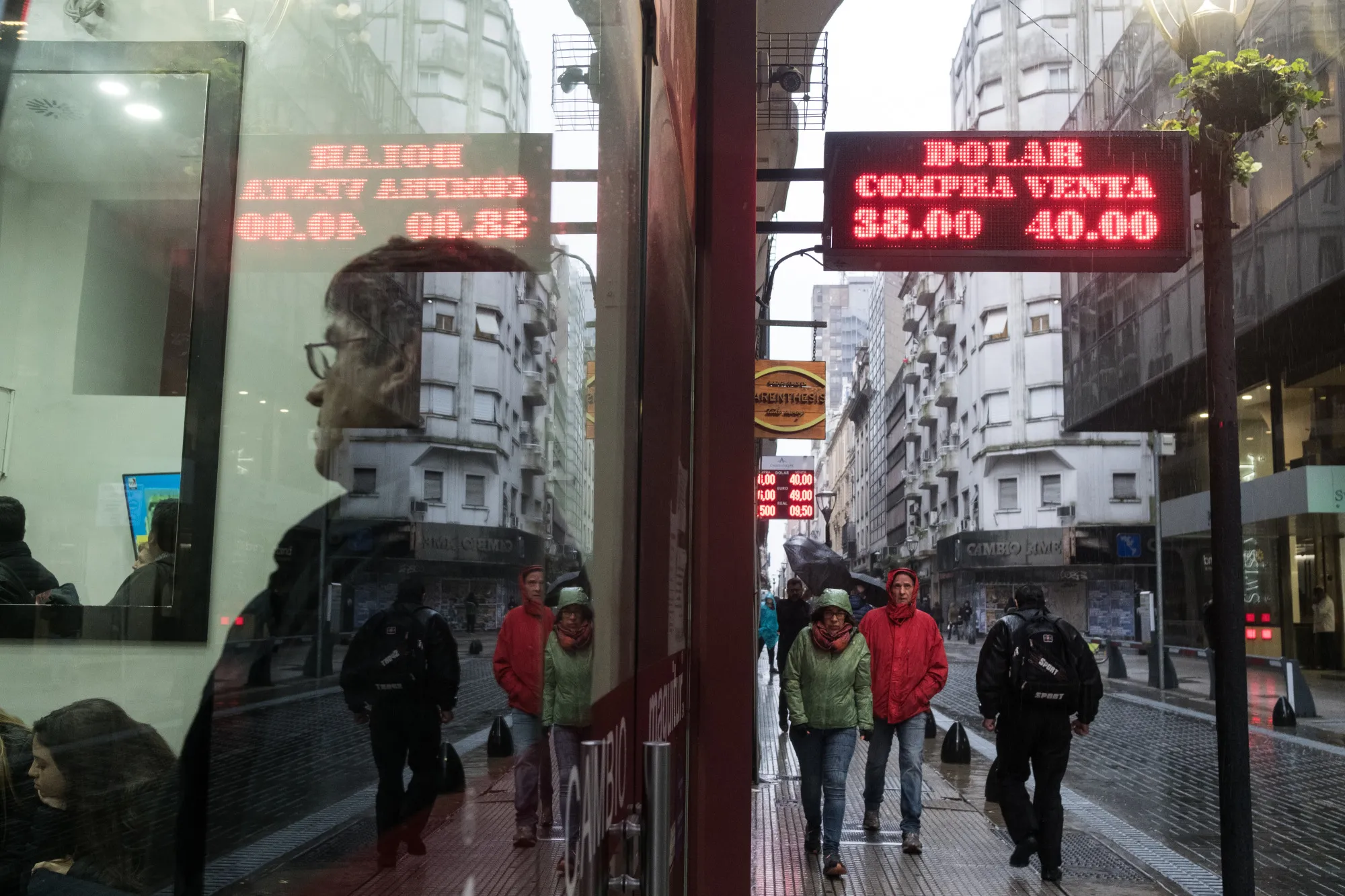 A sign displaying U.S. dollar exchange rates hangs as people wait inside of a currency exchange house in Buenos Aire.