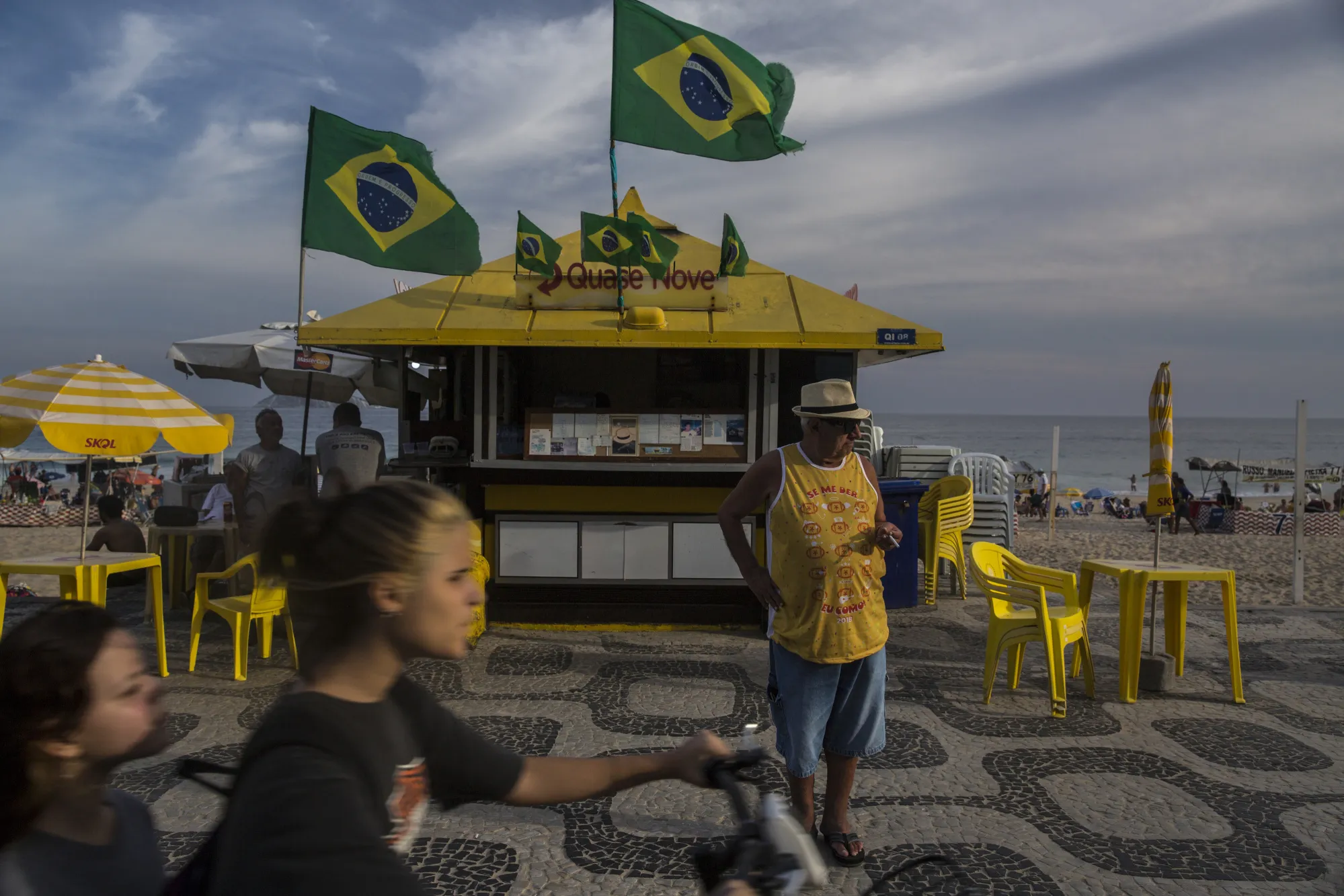 People pass Brazilian flags flying above a kiosk on Ipanema Beach in Rio de Janeiro.