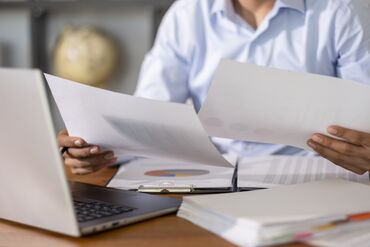 Businessman reviewing paperwork and using laptop at work
