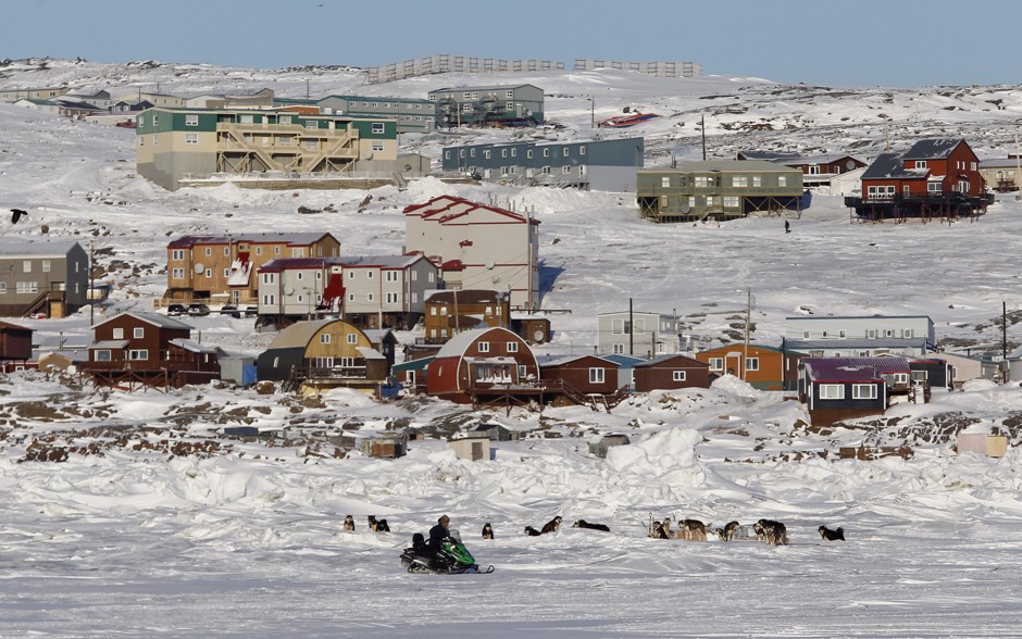 A snowmobiler rides past sled dogs on Frobisher Bay in Iqaluit, Nunavut, Canada.  