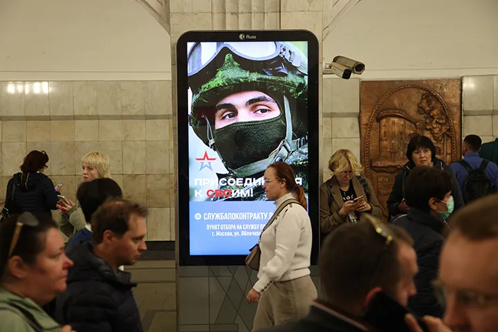 Passengers walk past a billboard advertising contract service in the army, at a subway station in Moscow.