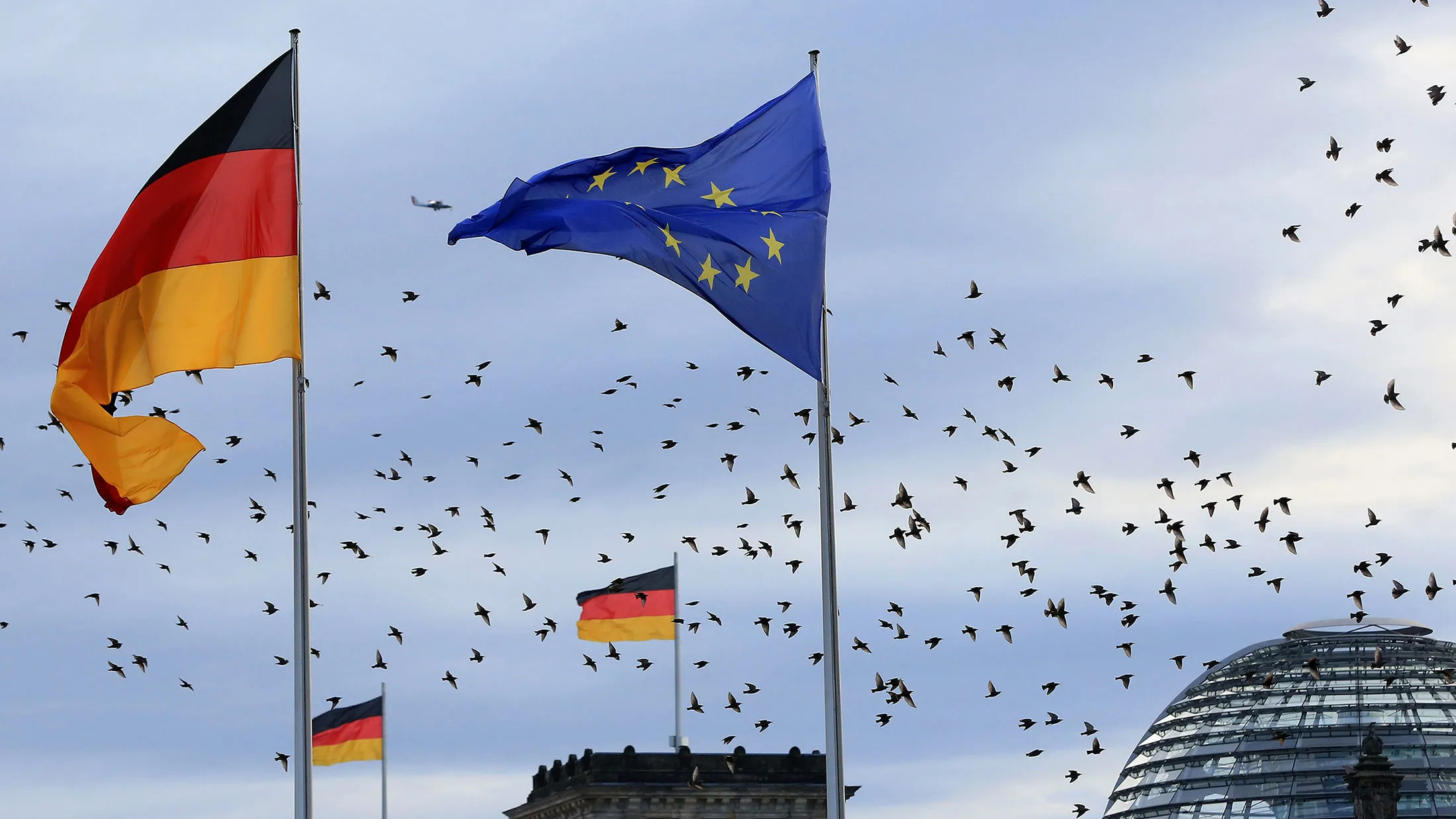 The German national flag flies beside a European Union (EU) flag as a flock of birds take flight over the Reichstag building in Berlin, Germany, on Nov. 18, 2016.
