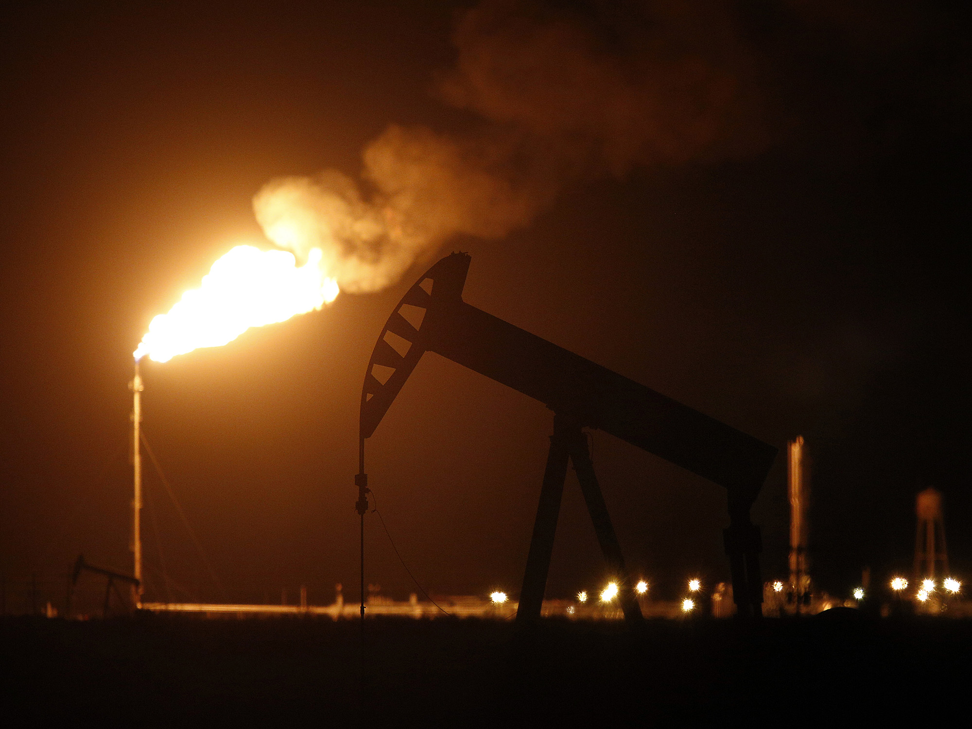 The silhouette of an electric oil pump jack is seen near a flare at night in the oil fields surrounding Midland, Texas.