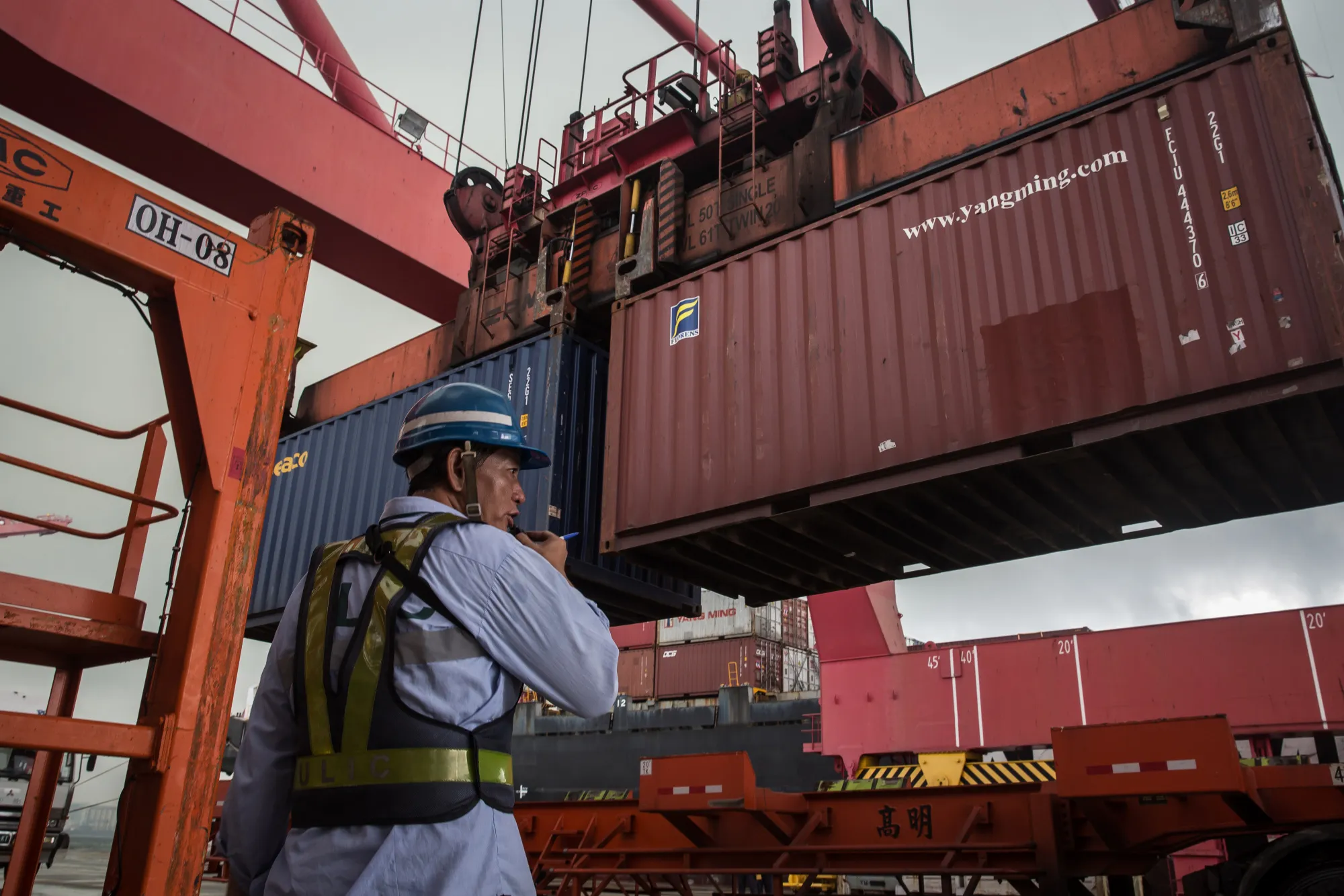 An employee observes a shipping container being lifted by a gantry crane at the Port of Kaohsiung in Kaohsiung, Taiwan.