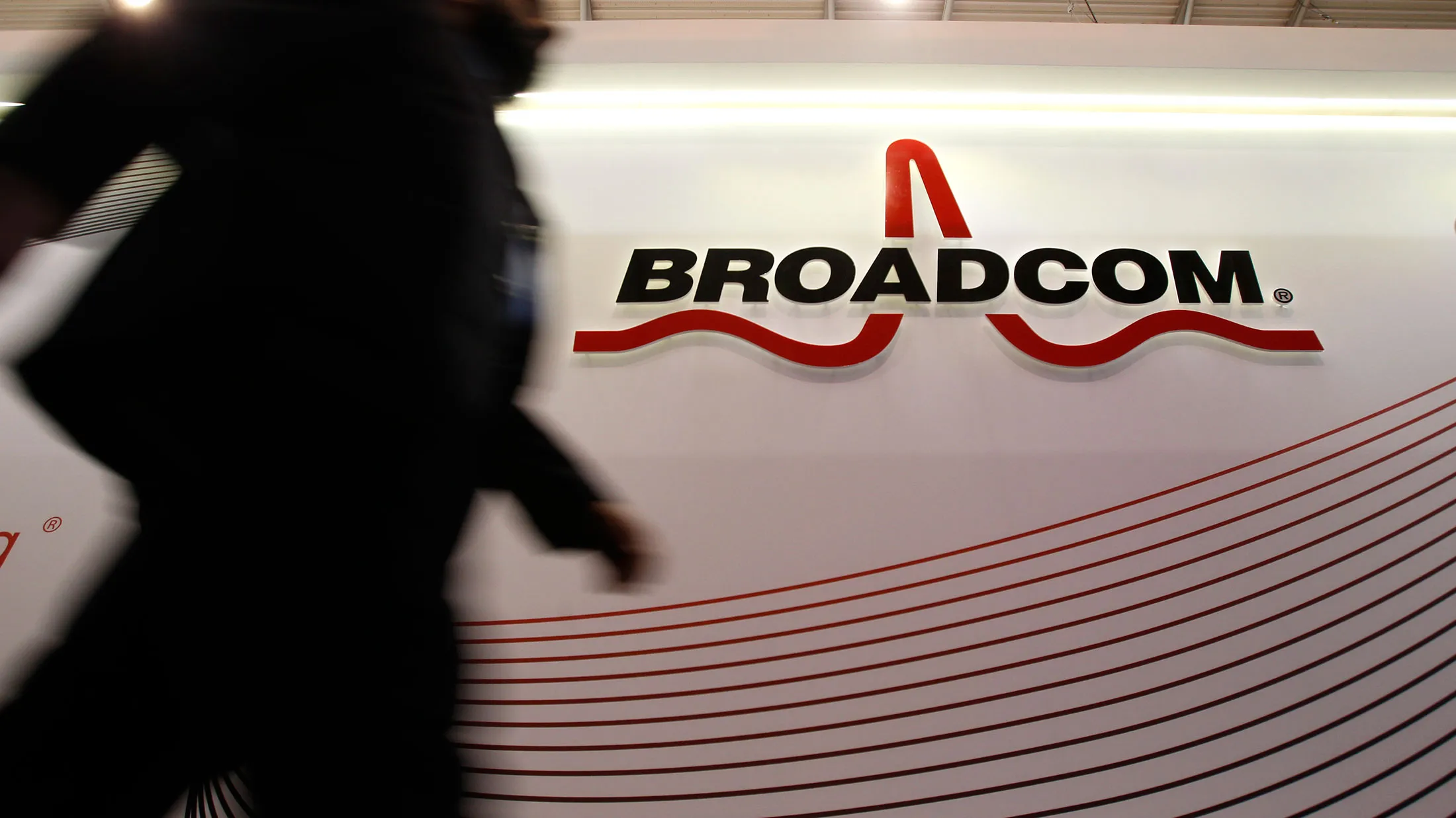 An attendee passes the Broadcom Corp. pavilion on day two of the Mobile World Congress in Barcelona, Spain, on Feb. 25, 2014.
