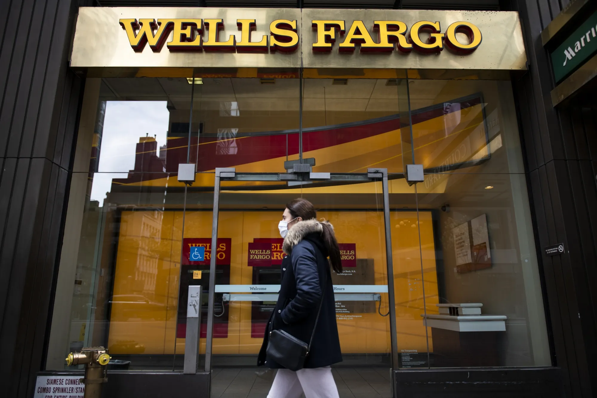 A person wearing a protective mask walks past a temporarily closed Wells Fargo branch.&nbsp;