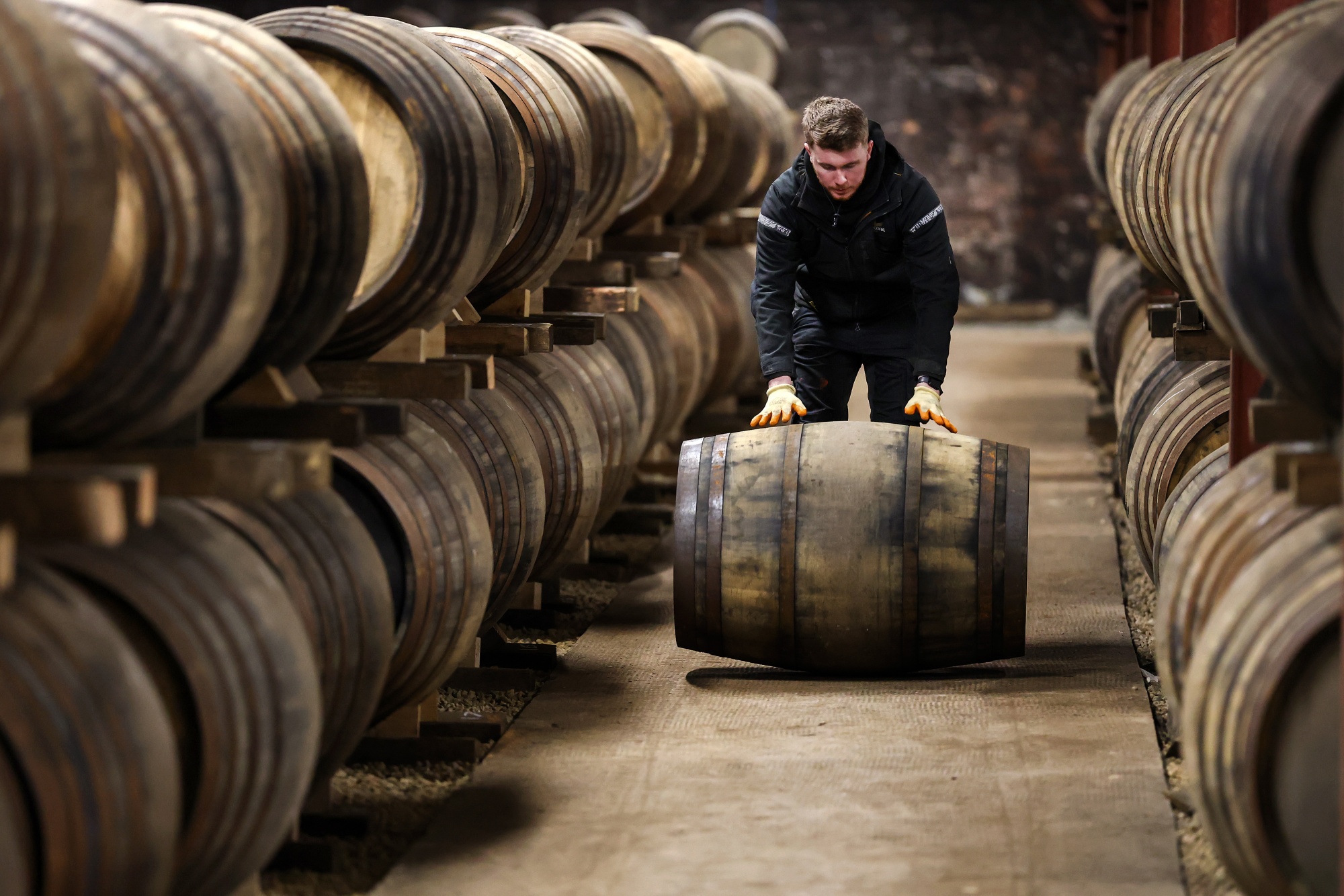 A member of staff rolls a barrel of whisky at a distillery in Glasgow, Scotland. Photographer: Jeff J Mitchell/Getty Images
