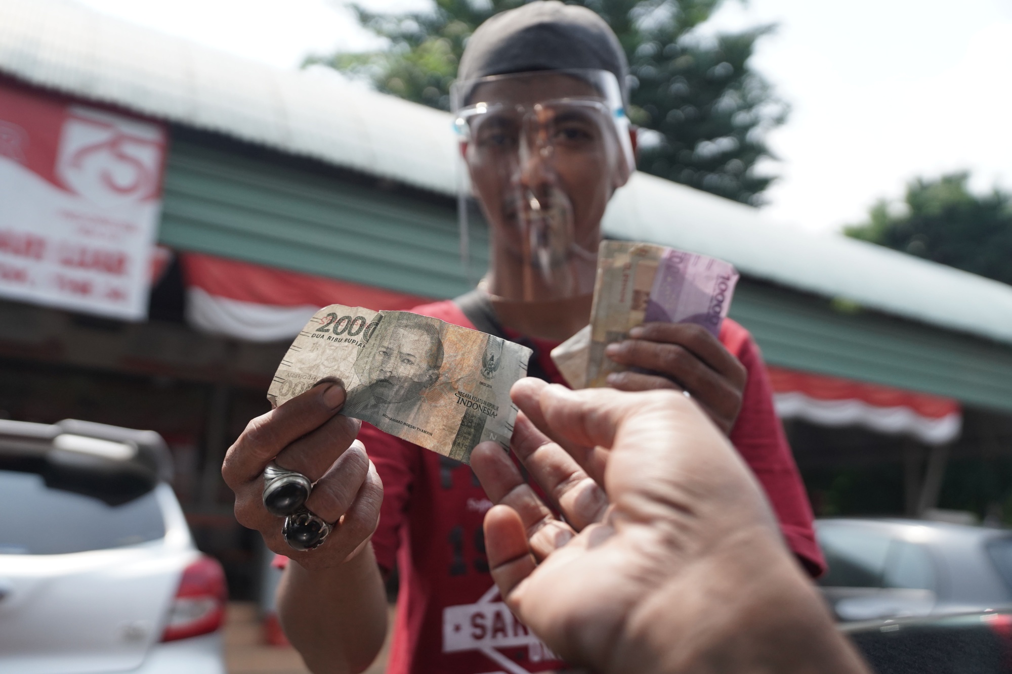 A parking attendant wearing a protective face mask handles Indonesian rupiah banknotes in Jakarta.