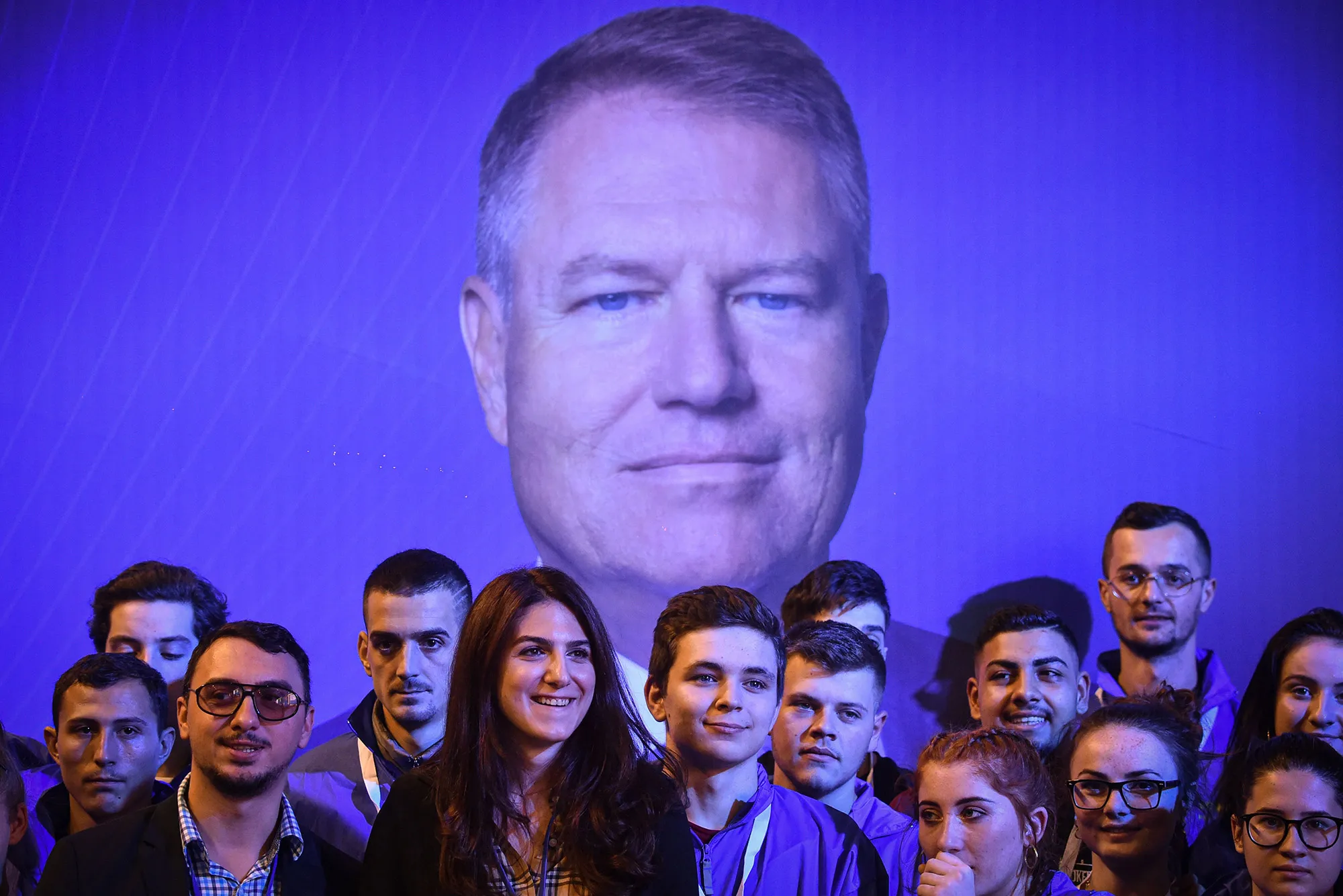 Supporters of Romanian President Klaus Iohannis stand in front of his picture at an electoral meeting. 