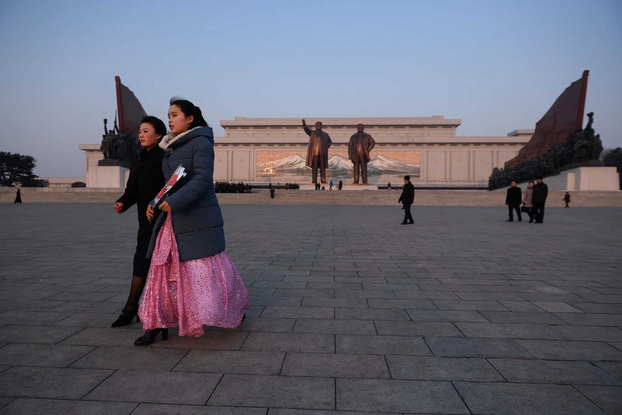 A woman holding flowers walks before the statues of late North Korean leaders Kim Il Sung and Kim Jong Il in Pyongyang.