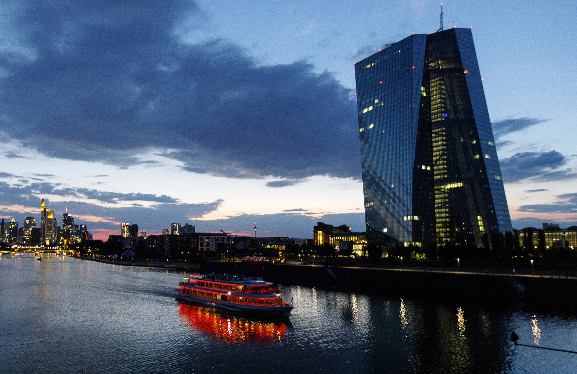 A sightseeing boat travels on the River Main past the European Central Bank (ECB) skyscraper headquarters, right, at dusk in Frankfurt.