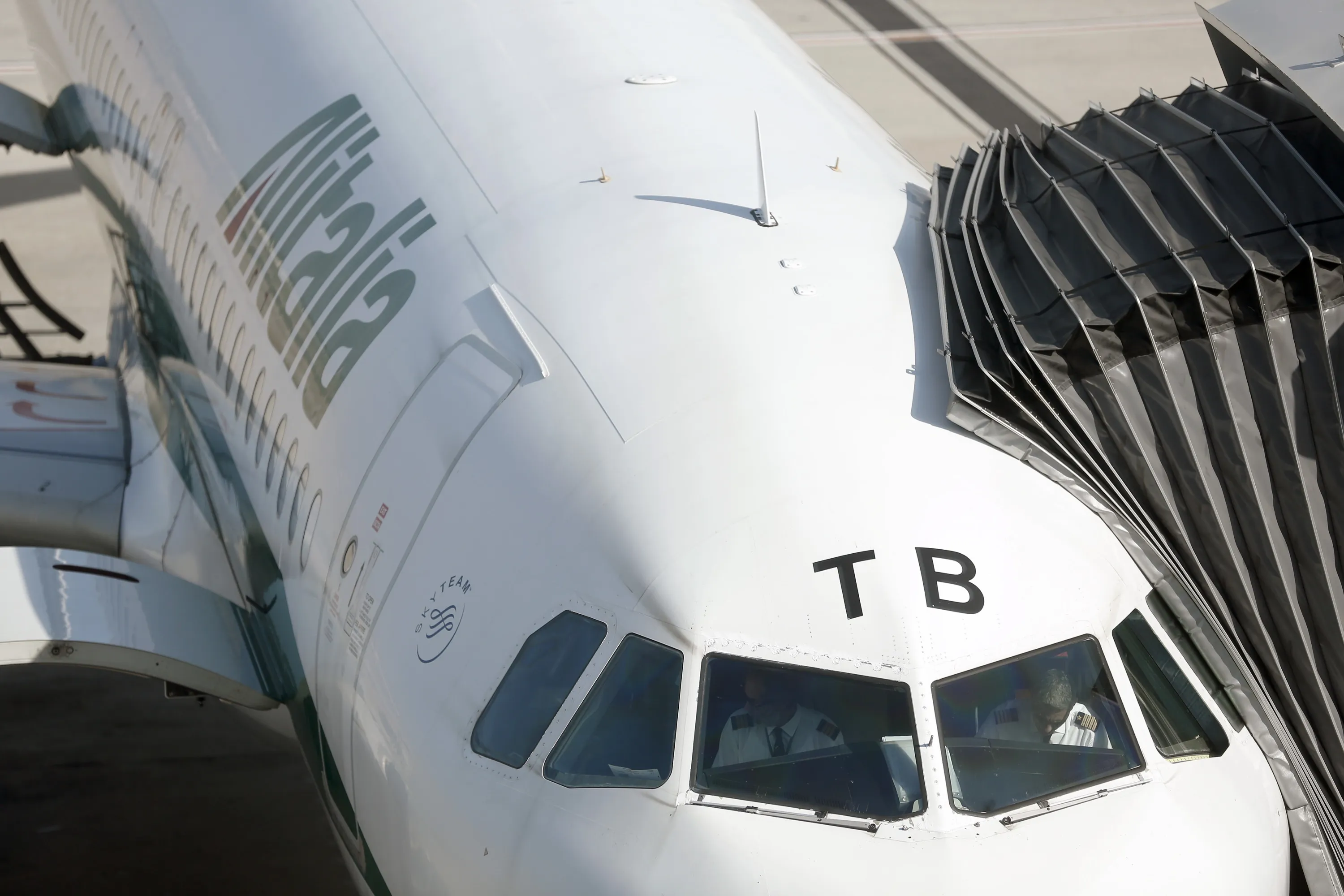Pilots sit inside the cockpit of an Alitalia SpA aircraft as it stands at a departure gate at Fiumicino airport in Rome